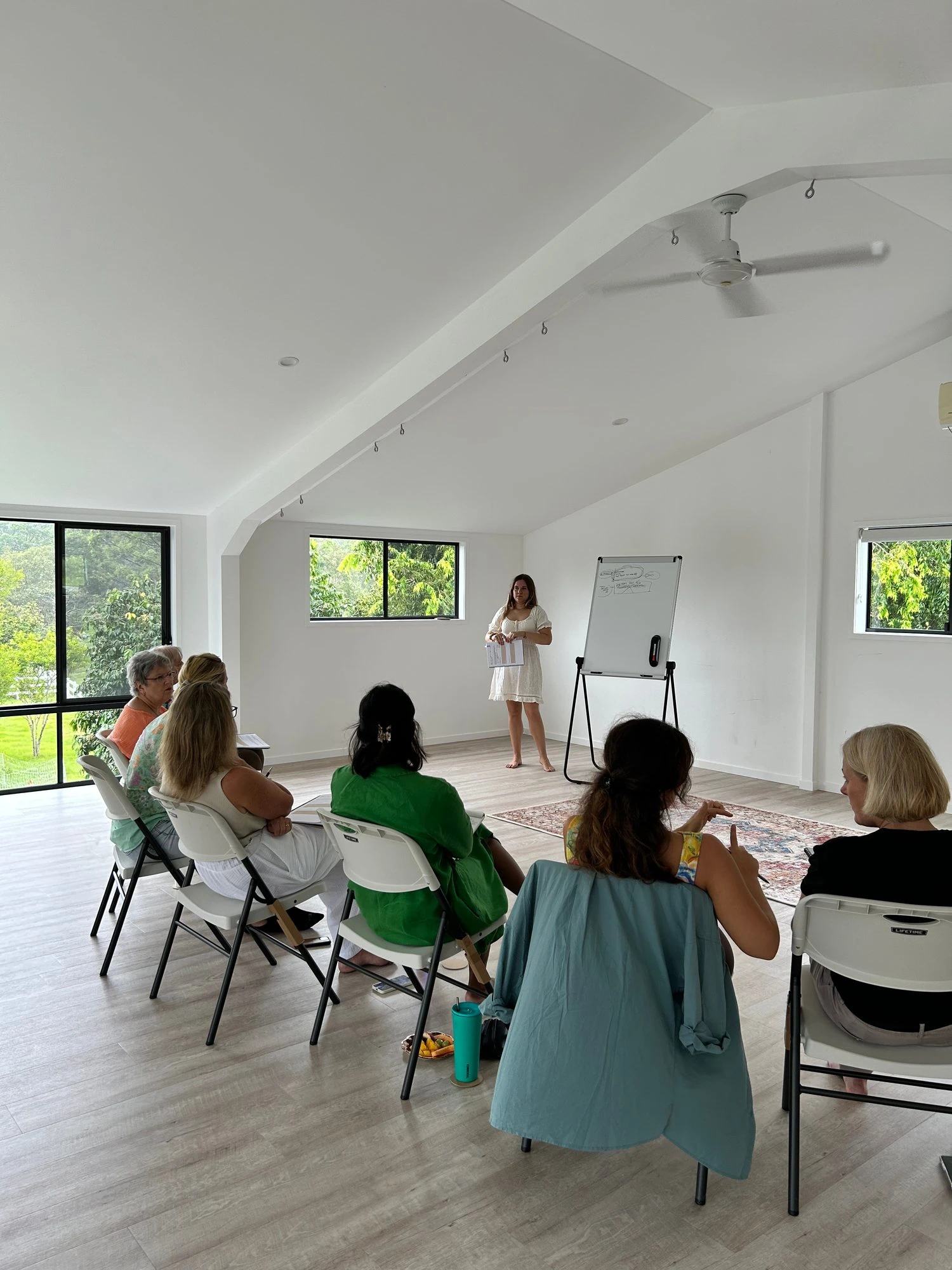 Merce teaching a small group at a whiteboard in a bright, light-filled room