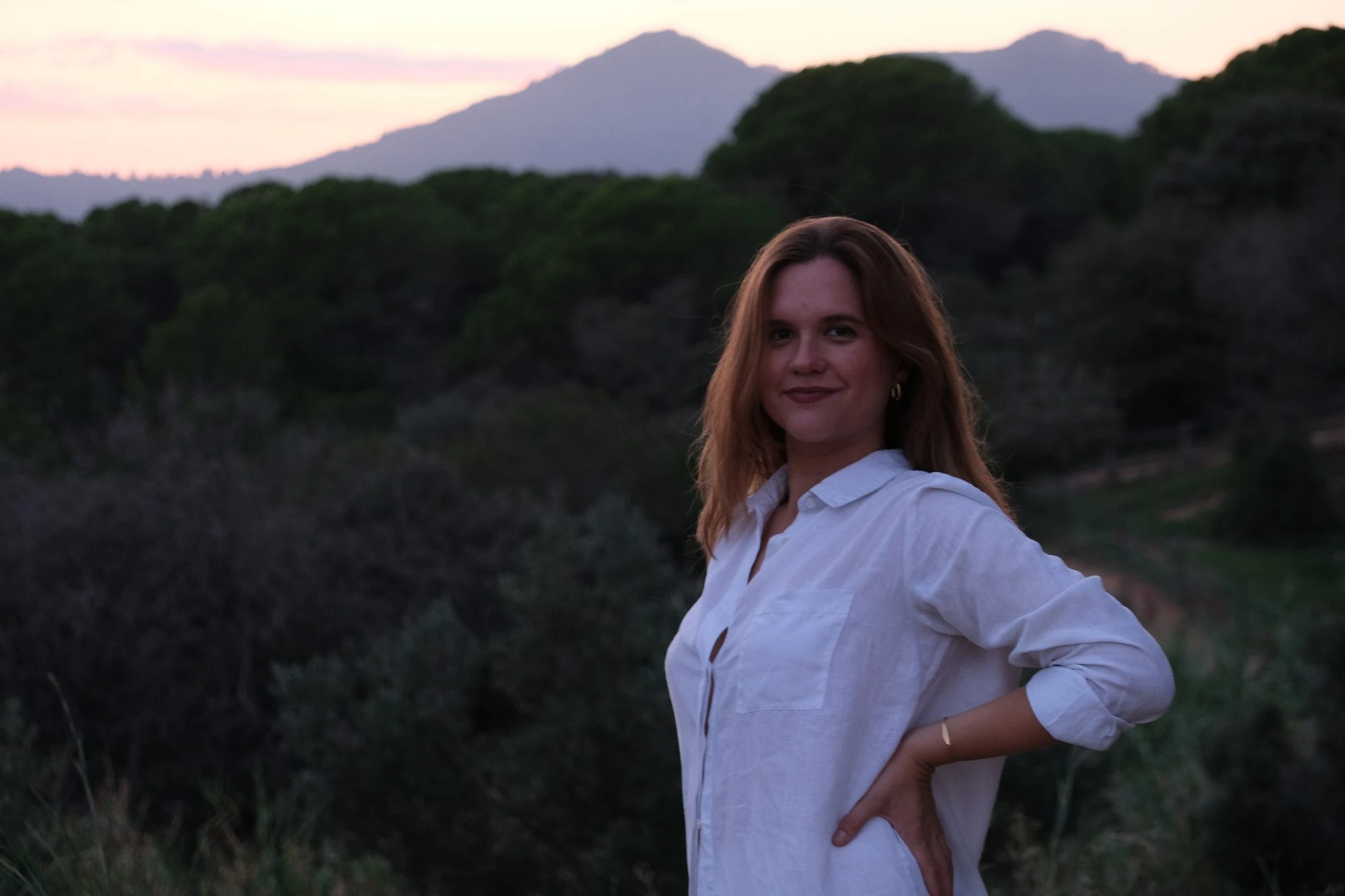 Merce smiling at sunset, with green hills and mountains behind her