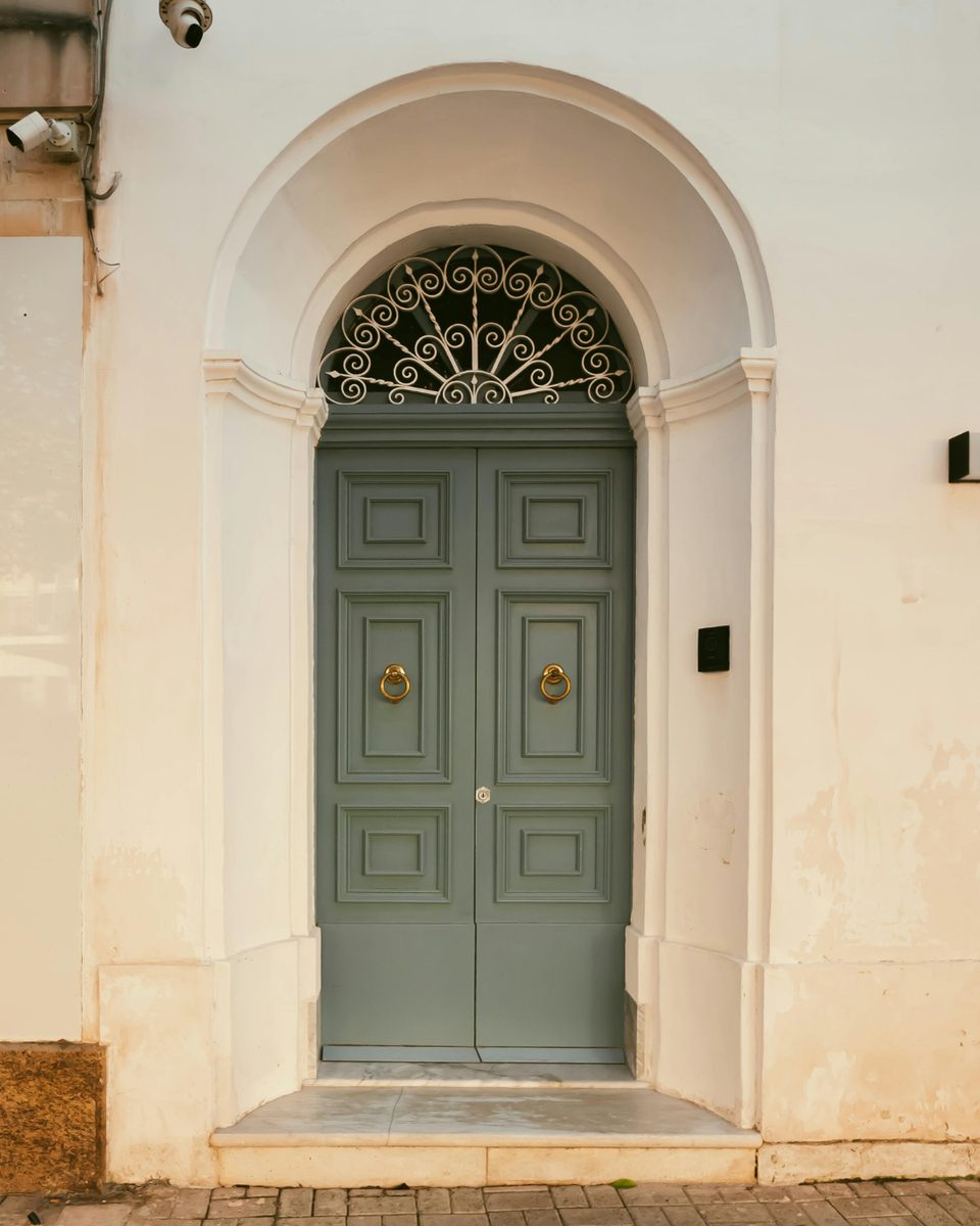 A sage-green Mediterranean doorway in a sunlit facade